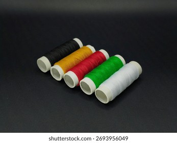 Five sewing thread spools in black, yellow, red, green, and white standing upright, symbolizing African unity and color diversity