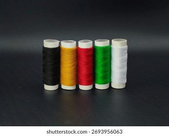 Five sewing thread spools in black, yellow, red, green, and white standing upright, symbolizing African unity and color diversity