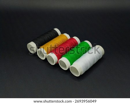 Five sewing thread spools in black, yellow, red, green, and white standing upright, symbolizing African unity and color diversity