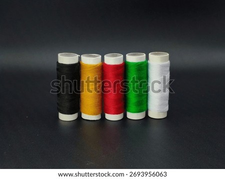 Five sewing thread spools in black, yellow, red, green, and white standing upright, symbolizing African unity and color diversity