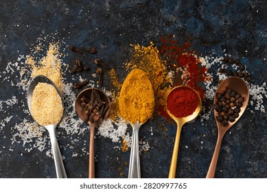 Five Spoons Filled With Different Spices: Garlic Powder, Cloves, Turmeric, Paprika, And Whole Black Peppercorns Arranged On A Dark Surface
