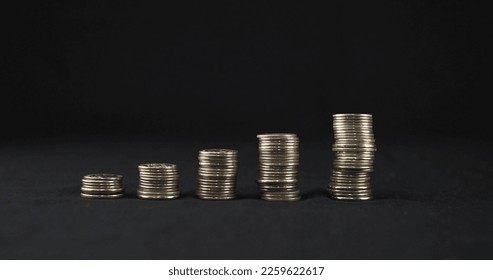 Five stacks of coins stand in a row on a black background. Stacks of coins stand on a black background in ascending order. The concept of increasing financial income. - Shutterstock ID 2259622617