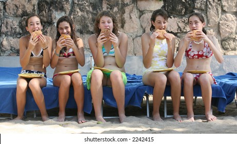 Five teenage girls eating hamburgers on the beach