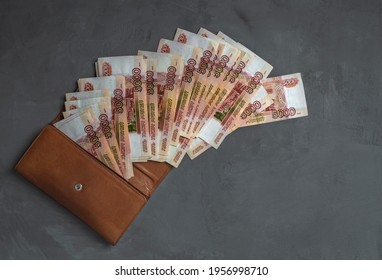 Five thousandth bills fanned out on a gray concrete background and a brown wallet. - Shutterstock ID 1956998710