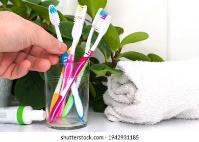 Five Toothbrushes In A Glass Cup Mouthwash A Tube Of Toothpaste And A Rolled Up Towel On The Dressing Table Against A Backdrop Of Green Foliage A Man Takes A Toothbrush Out Of  Glass. High Quality Pho