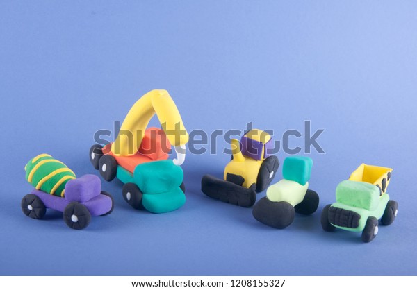 Five toy building machines made of\
colorful modeling clay staying on purple\
background