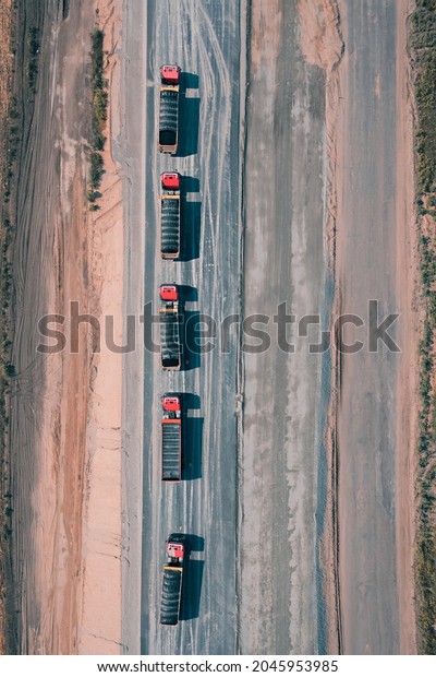 Five\
trucks with cargo are driving along an asphalt road in the middle\
of desert. Aerial drone shot. Trucks carry building materials for\
construction of the road. Top view drone\
shot.