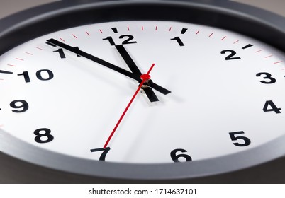It's five to twelve, the clock is ticking. Modern white clock shows the time 5 before 12. Close up to a wall clock, with five minutes to twelve o'clock. Time running out to avoid the climate change