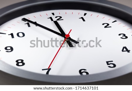 It's five to twelve, the clock is ticking. Modern white clock shows the time 5 before 12. Close up to a wall clock, with five minutes to twelve o'clock. Time running out to avoid the climate change