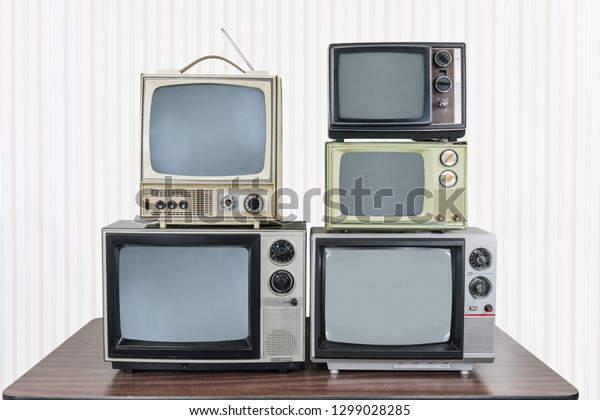 Five\
vintage televisions stacked on old wood\
table.