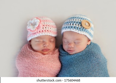 Five week old sleeping boy and girl fraternal twin newborn babies. They are wearing crocheted pink and blue striped hats.