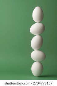Five white eggs balancing in a vertical line on green background forming clean minimal concept of fragile stability and precise harmony