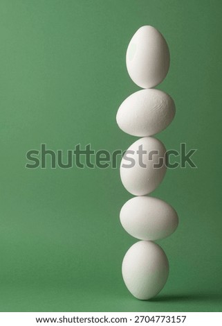 Five white eggs balancing in a vertical line on green background forming clean minimal concept of fragile stability and precise harmony