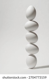 Five white eggs balancing vertically on white background forming airy minimal scene that highlights fragile balance and gentle harmony