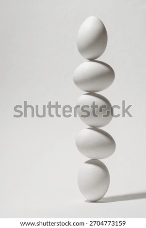 Five white eggs balancing vertically on white background forming airy minimal scene that highlights fragile balance and gentle harmony