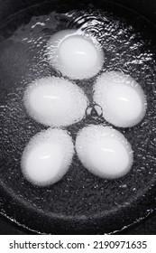 Five White Eggs In A Pot Of Boiling Water Against A Black Background. Top View. 