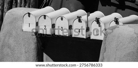 five white mailboxes numbered one through five situated between two adobe style posts all closed showing their numbers horizontal black and white image representing the postal service and snail mail