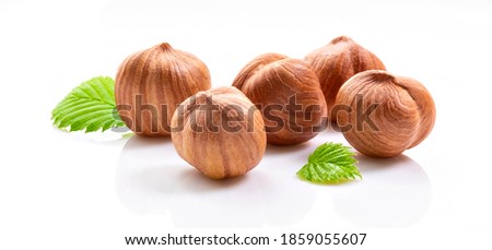 Five whole kernels of hazelnut and two leaves on white background