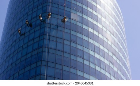 Five Window Washers Hanging With Ropes Outside Blue Glass Modern Building. Risky Job, Dangerous Work Concepts