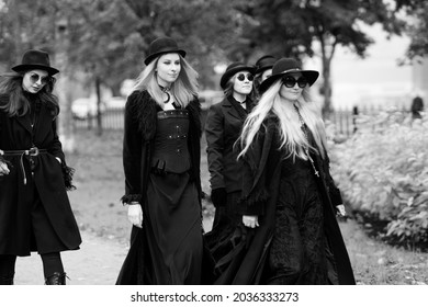 Five Women As Witches Go To The Sabbath, A Group Of Witches Or Goths In Black Clothes And Hats Go Down The Street