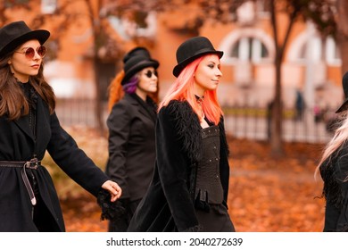 Five Women As Witches Go To The Sabbath, A Group Of Witches Or Goths In Black Clothes And Hats Go Down The Street
