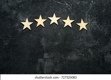 Five wooden stars located in the form of an arch or arc in the upper part of a dark cement background. Conceptual of service rating and quality of trade. Top view, copy space for your text.