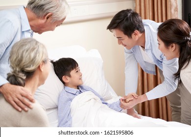 Five Year Old Asian Child Lying In Bed In Hospital Ward Gets A Visit From Parents And Grandparents