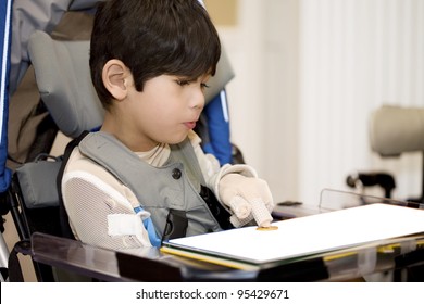 Five year old disabled boy studying in wheelchair, pointing at object on book