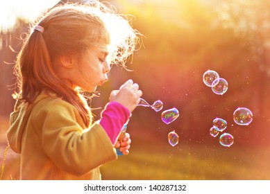 Five years old caucasian child girl blowing soap bubbles outdoor at sunset - happy carefree childhood