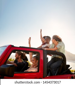 Five Young Adult Friends On A Road Trip Driving In An Open Top Jeep By The Sea