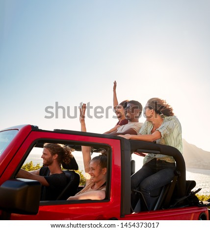 Five young adult friends on a road trip driving in an open top jeep by the sea