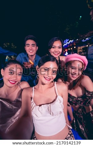 Five young friends take fun selfies while partying at a nightclub or bar. 5 people having a great time together. Nightlife scene.