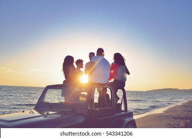 Five Young People Having Fun In Convertible Car At The Beach At Sunset.