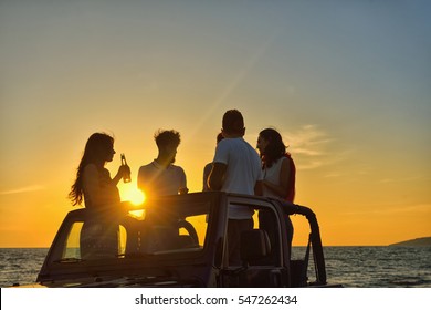 Five Young People Having Fun In Convertible Car At The Beach At Sunset.