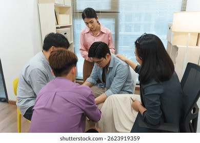 Five young professionals engage in a collaborative effort, with one person seated at a desk while others provide assistance and guidance in a bright office setting.