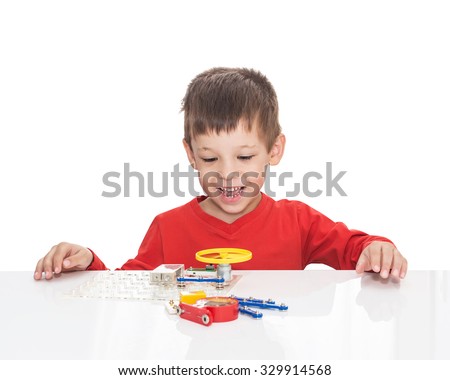 The five-year-old boy sits at a white table and plays an electronic designer (meccano, constructor) starts the propeller,  isolated on a white background
