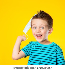 A Five-year-old Child Is Happy, Waving A Medical Mask In Connection With The End Of The Pandemic. The End Of The Coronavirus Epidemic. The Boy Laughs, Is Happy, And Smiles. On Yellow Background.