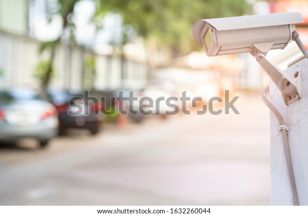 Fix CCTV cameras are\
installed with poles in the parking lot. Old Security CCTV camera\
or surveillance system on the white wall with blurred of the car\
background.