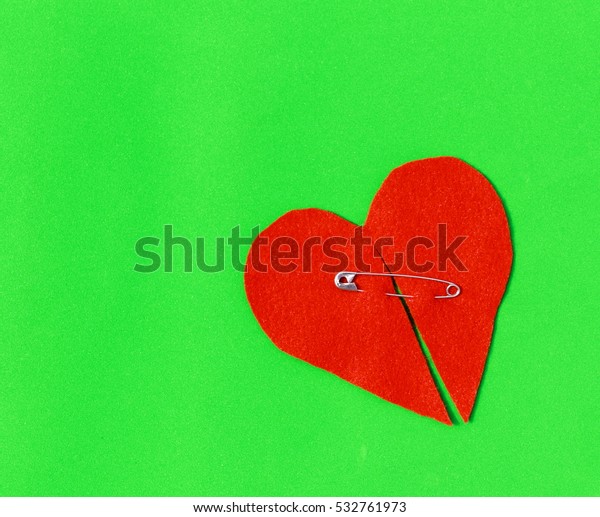 Fixed broken heart. Felt broken heart fixed\
with safety pin on green background. \
