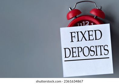 FIXED DEPOSITS - words on a white piece of paper on a gray background. Red alarm clock with white piece of paper. Business concept