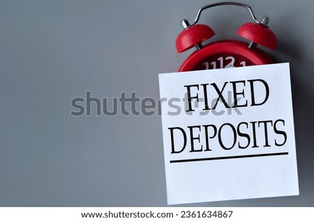 FIXED DEPOSITS - words on a white piece of paper on a gray background. Red alarm clock with white piece of paper. Business concept
