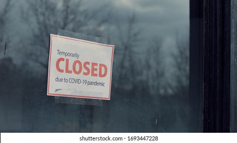 FIXED view of a Temporary closed due COVID-19 pandemic sign hanging on a window. Coronavirus pandemic, small business shutdown