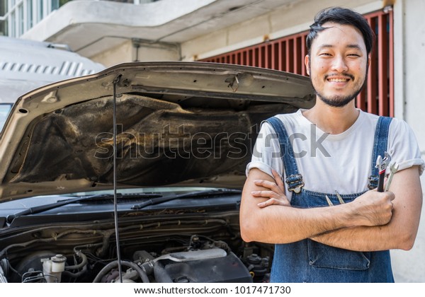Fixing car engine in automobile repair garage.\
Handsome mechanics in uniform are repairing car while working in\
auto service