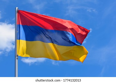 The flag of Armenia is a rectangular banner consisting of horizontal red, blue and orange stripes on a background of blue sky during the summer day.
