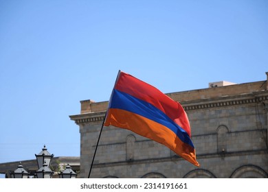 The flag of Armenia waving with the Republic Square building in the background