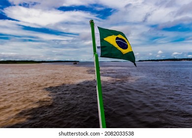 Flag Of Brazil Hoisted On Mast. And The Meeting Of The Negro River With The Solimões Forming The Amazon River.