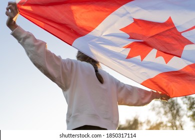 The flag of Canada in the hands of a person. Canadian symbol against the backdrop of a beautiful sunset. Pride and independence
