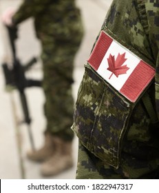 Flag Of Canada On The Military Uniform And Soldier With Weapon On The Background. Canadian Soldiers. Canadian Army. Remembrance Day. Canada Day.