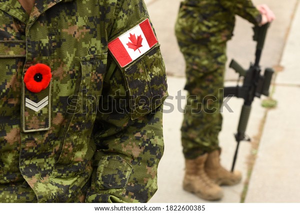 Flag of Canada on the military uniform and soldier\
with weapon on the background. Canadian soldiers. Canadian Army.\
Remembrance Day.Poppy day.\

