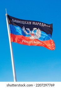 Flag Of Donetsk People's Republic (DPR Or DNR) With Coat Of Arms In The Center. Vertical Against Blue Sky Background. War In Eastern Ukraine (Donbas) Concept. 